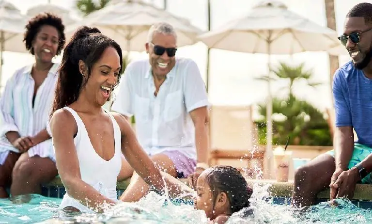 Family enjoying playful moments in a pool under sunny skies.