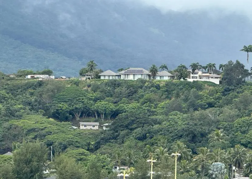 Scenic view of houses nestled among lush green hills with mountains in the background.