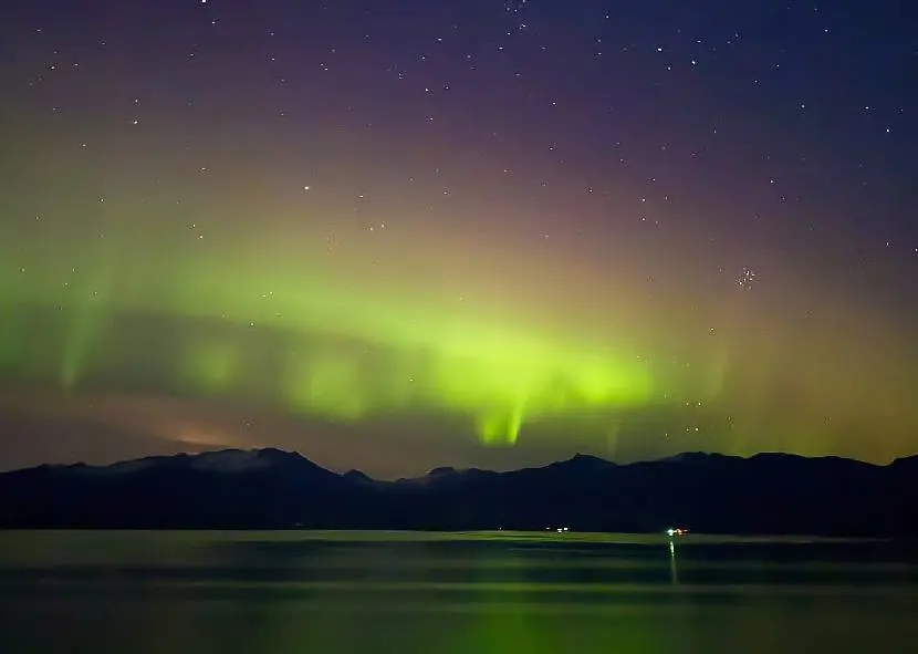 Vibrant green northern lights shimmering over dark mountains and calm water.